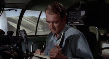 Movie still from “The Flight of the Phoenix” (1965), directed by Robert Aldrich – An older man writing on a piece of paper in an airplane cockpit; Medium shot, Over the shoulder angle