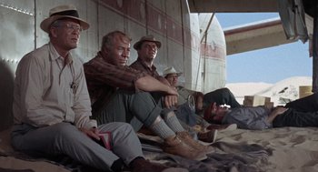 Movie still from “The Flight of the Phoenix” (1965), directed by Robert Aldrich – A group of men sitting next to each other on the ground; Wide shot, Low angle