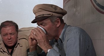 Movie still from “The Flight of the Phoenix” (1965), directed by Robert Aldrich – A man wearing a hat drinking a cup of coffee; Close Up shot, High angle