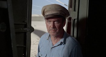 Movie still from “The Flight of the Phoenix” (1965), directed by Robert Aldrich – A man wearing a hat standing in front of a door; Close Up shot, Low angle