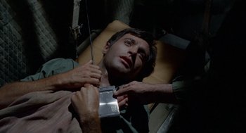 Movie still from “The Flight of the Phoenix” (1965), directed by Robert Aldrich – A man laying in a hospital bed while being examined by a doctor; Close Up shot, Overhead angle