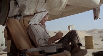 Movie still from “The Flight of the Phoenix” (1965), directed by Robert Aldrich – A man sitting in a chair writing on a piece of paper; Medium shot, Low angle