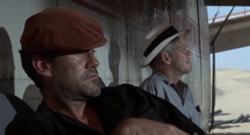 Movie still from “The Flight of the Phoenix” (1965), directed by Robert Aldrich – Two men wearing hats are sitting next to each other; Close Up shot, Low angle