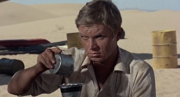 Movie still from “The Flight of the Phoenix” (1965), directed by Robert Aldrich – A man drinking from a metal cup in the desert; Close Up shot, Low angle