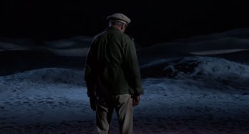 Movie still from “The Flight of the Phoenix” (1965), directed by Robert Aldrich – An older man in a green jacket is standing in the dark; Wide shot, High angle