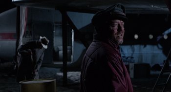 Movie still from “The Flight of the Phoenix” (1965), directed by Robert Aldrich – A man wearing a hat standing in the dark; Medium shot, Over the shoulder angle