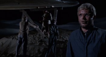 Movie still from “The Flight of the Phoenix” (1965), directed by Robert Aldrich – A man standing in front of an airplane at night; Medium shot, Over the shoulder angle