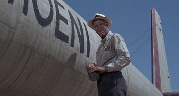 Movie still from “The Flight of the Phoenix” (1965), directed by Robert Aldrich – An older man in a hat standing in front of an airplane; Wide shot, Low angle
