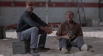 Movie still from “The Flight of the Phoenix” (1965), directed by Robert Aldrich – A couple of men sitting on top of a sandy beach; Wide shot, Low angle