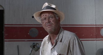 Movie still from “The Flight of the Phoenix” (1965), directed by Robert Aldrich – An older man wearing a hat and glasses in front of a wall; Close Up shot, Low angle