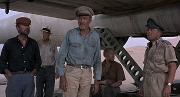 Movie still from “The Flight of the Phoenix” (1965), directed by Robert Aldrich – A man wearing a hat standing next to two other men; Medium shot, Low angle