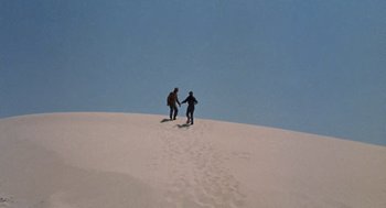 Movie still from “The Flight of the Phoenix” (1965), directed by Robert Aldrich – Two people are walking up a sand dune; Extreme Wide shot, High angle