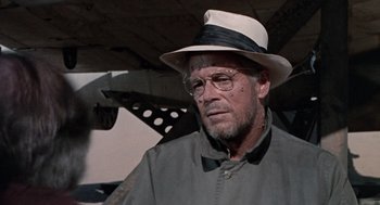 Movie still from “The Flight of the Phoenix” (1965), directed by Robert Aldrich – An older man wearing a hat and glasses; Close Up shot, Over the shoulder angle