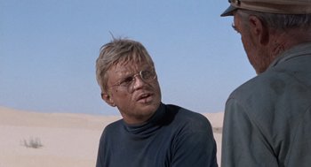 Movie still from “The Flight of the Phoenix” (1965), directed by Robert Aldrich – A man in a black shirt is talking to another man; Close Up shot, Over the shoulder angle