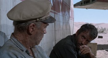 Movie still from “The Flight of the Phoenix” (1965), directed by Robert Aldrich – Two men sitting next to each other on the side of a building; Medium shot, Low angle