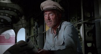 Movie still from “The Flight of the Phoenix” (1965), directed by Robert Aldrich – A man in a hat is reading a newspaper; Medium shot, Low angle