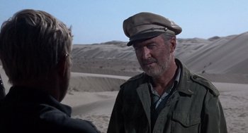 Movie still from “The Flight of the Phoenix” (1965), directed by Robert Aldrich – A man wearing a hat talking to another man in the desert; Close Up shot, Over the shoulder angle