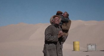 Movie still from “The Flight of the Phoenix” (1965), directed by Robert Aldrich – A man standing in the sand with two other men; Medium shot, Low angle