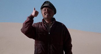 Movie still from “The Flight of the Phoenix” (1965), directed by Robert Aldrich – An older man giving a thumbs up while standing in the sand dunes; Medium shot, Low angle