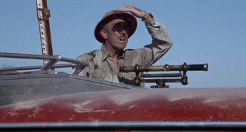 Movie still from “The Flight of the Phoenix” (1965), directed by Robert Aldrich – A man with a red hat is in the back of a red truck; Close Up shot, Low angle