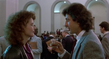 Movie still from “The Fly” (1986), directed by David Cronenberg – A man and a woman holding a glass of wine in front of a crowd; Medium shot, Over the shoulder angle