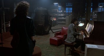 Movie still from “The Fly” (1986), directed by David Cronenberg – A man sitting in a chair next to a woman; Wide shot, Over the shoulder angle