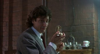Movie still from “The Fly” (1986), directed by David Cronenberg – A man in a gray suit holding a glass object; Close Up shot, Low angle