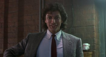 Movie still from “The Fly” (1986), directed by David Cronenberg – A man in a suit and tie smiling for the camera; Close Up shot, Low angle
