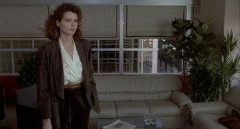 Movie still from “The Fly” (1986), directed by David Cronenberg – A woman standing in front of a couch in a living room; Medium shot, Over the shoulder angle