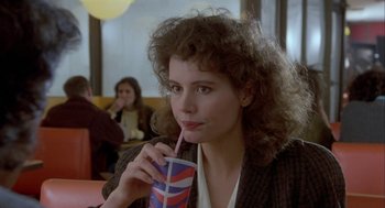 Movie still from “The Fly” (1986), directed by David Cronenberg – A woman sitting at a table with a drink in her hand; Close Up shot, Over the shoulder angle