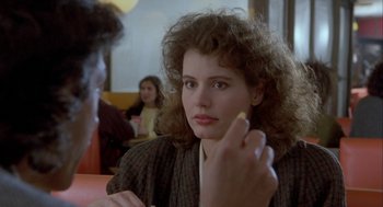 Movie still from “The Fly” (1986), directed by David Cronenberg – A woman sitting at a table in front of other people; Close Up shot, Over the shoulder angle