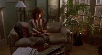 Movie still from “The Fly” (1986), directed by David Cronenberg – A woman sitting on top of a couch in a living room; Wide shot, High angle