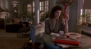 Movie still from “The Fly” (1986), directed by David Cronenberg – A woman sitting at a table in a living room; Wide shot, Over the shoulder angle