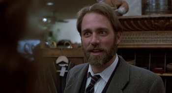 Movie still from “The Fly” (1986), directed by David Cronenberg – A man in a suit and tie smiling for the camera; Close Up shot, Over the shoulder angle