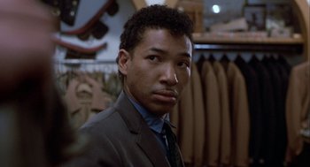 Movie still from “The Fly” (1986), directed by David Cronenberg – A man wearing a suit and tie in a store; Close Up shot, Over the shoulder angle