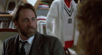 Movie still from “The Fly” (1986), directed by David Cronenberg – A man in a suit and tie in front of clothes; Close Up shot, Over the shoulder angle