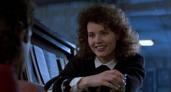 Movie still from “The Fly” (1986), directed by David Cronenberg – A woman sitting in a chair holding a glass; Close Up shot, Over the shoulder angle