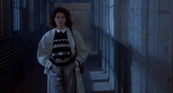 Movie still from “The Fly” (1986), directed by David Cronenberg – A woman standing in a dark hallway holding a purse; Medium shot, Low angle