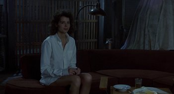 Movie still from “The Fly” (1986), directed by David Cronenberg – A woman sitting on top of a brown couch in a room; Medium shot, Over the shoulder angle