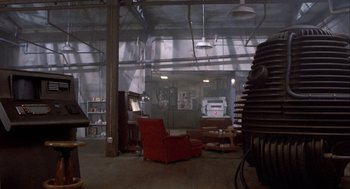 Movie still from “The Fly” (1986), directed by David Cronenberg – An empty room with a red chair and a large window; Extreme Wide shot, High angle