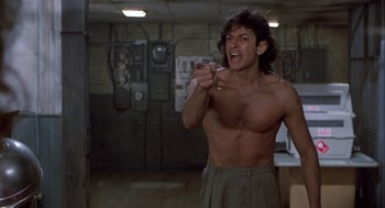 Movie still from “The Fly” (1986), directed by David Cronenberg – A shirtless man pointing at something in a room; Medium shot, Low angle