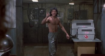 Movie still from “The Fly” (1986), directed by David Cronenberg – A shirtless man is pointing to the camera; Medium shot, Low angle