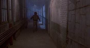 Movie still from “The Fly” (1986), directed by David Cronenberg – A man walking down a hallway in a building; Wide shot, High angle