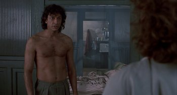 Movie still from “The Fly” (1986), directed by David Cronenberg – A man standing in front of a mirror in a room; Medium shot, Over the shoulder angle