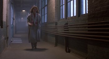 Movie still from “The Fly” (1986), directed by David Cronenberg – A woman in a long coat walking down a hallway; Wide shot, Low angle