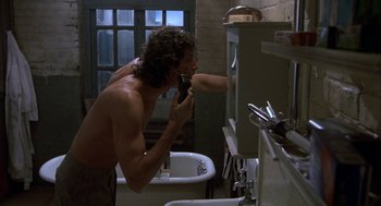 Movie still from “The Fly” (1986), directed by David Cronenberg – A man shaving in a bathroom while another man watches; Medium shot, Low angle
