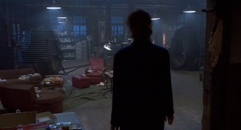 Movie still from “The Fly” (1986), directed by David Cronenberg – A man standing in a dark room in front of a fire place; Wide shot, Over the shoulder angle