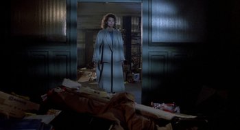 Movie still from “The Fly” (1986), directed by David Cronenberg – A woman standing in a room with a pile of trash; Wide shot, Low angle