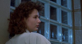 Movie still from “The Fly” (1986), directed by David Cronenberg – A woman with curly brown hair is standing in front of a window; Close Up shot, Low angle