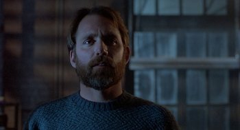 Movie still from “The Fly” (1986), directed by David Cronenberg – A man with a goatee and a beard stares into the distance; Close Up shot, Over the shoulder angle